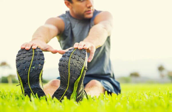 Man sitting on grass stretching forward to touch his toes with both hands, focusing on flexibility and fitness - Chiropractor Alpharetta GA